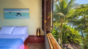 Un dormitorio con cama, un cuadro de delfines, una ventana con vista a palmeras y al mar.