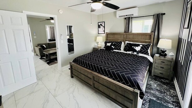 A bedroom with a bed, a ceiling fan, a nightstand, a dresser, a mirror, and a door. - #7 Heated Pool, Private Patio & Grill (Fort Lauderdale)