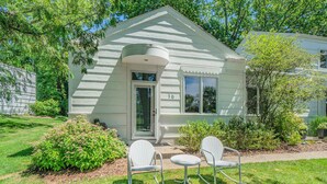A white single-story house with a number 16 on the door, two white rocking chairs, and a small garden area. - Sleepy Hollow Beach Resort, Terrace 16 – Family Fun on Lake Michigan! (South Haven)