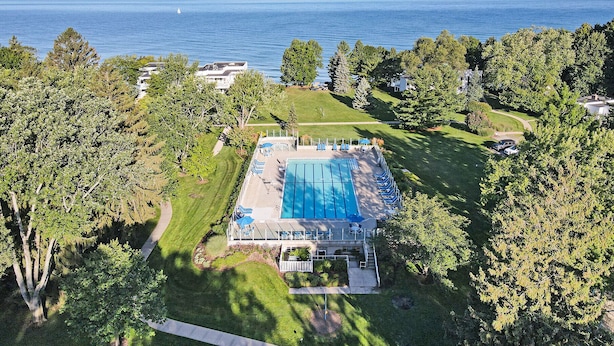 An aerial view of a property with a swimming pool surrounded by trees, a clear view of the sea, and a well-maintained lawn. - Sleepy Hollow Beach Resort, Terrace 16 – Family Fun on Lake Michigan! (South Haven)
