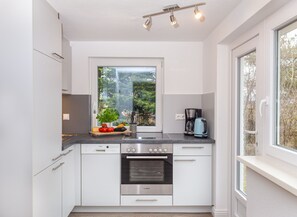 Una cocina moderna con armarios blancos, un horno Bosch, una cafetera y una ventana con vistas a árboles.