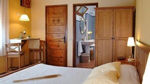 Un dormitorio con cama, armario de madera y baño visible a través de una puerta abierta.
