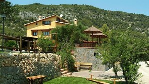 Una villa rústica con un muro de piedra, una terraza de madera y un comedor con bancos.
