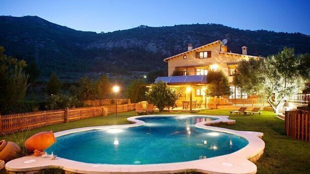 Una piscina con una casa al fondo, rodeada por una valla de madera y árboles.