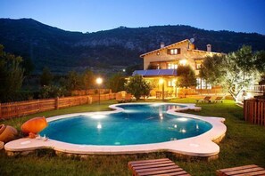 A pool with a house in the background, surrounded by a wooden fence and trees. - Self catering La Ginesta rural for 20 people (Sitges)