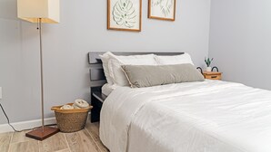 Et pænt møbleret soveværelse med seng, natbord, lampe og indrammede botaniske illustrationer på væggen.