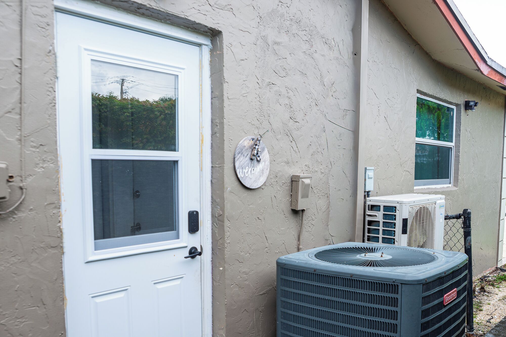 A house with a white door, a welcome sign, and an air conditioning unit.