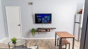 En moderne stue med et fladskærms-tv monteret på væggen, et træbord, en bænk, en sofa og en lille plante på et glastemperglasbord.