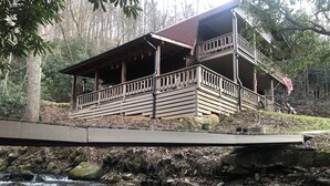 A wooden cabin with a balcony, situated by a flowing stream.
