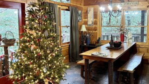 A cozy cabin interior with a wooden dining table, benches, a Christmas tree, and a chandelier.