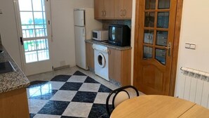 A compact kitchen with a washing machine, microwave, and a small refrigerator. There is a checkered floor and a wooden door with glass panels. - Upper floor housing (Verín)