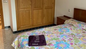 A bedroom with a large wooden wardrobe, a bed with a colorful floral bedspread, and a small bedside table. - Upper floor housing (Verín)