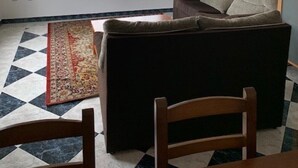 A room with a sofa, a chair, a patterned rug, and a window with a view of greenery. - Upper floor housing (Verín)