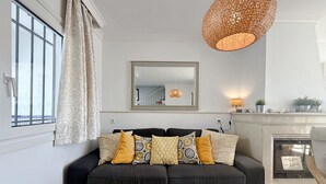 Un salon avec un canapé noir, une table basse blanche, un grand miroir et une cheminée.