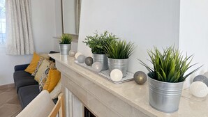 Un salon avec un canapé, des coussins, une cheminée et des plantes en pot sur le manteau de la cheminée.