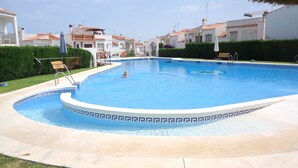 Une piscine dont le bord est revêtu de carrelage, entourée d’une haie basse et d’une terrasse dallée.