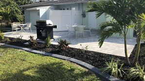 Een terras met een barbecue, zitplaatsen buiten en een kleine tuin.