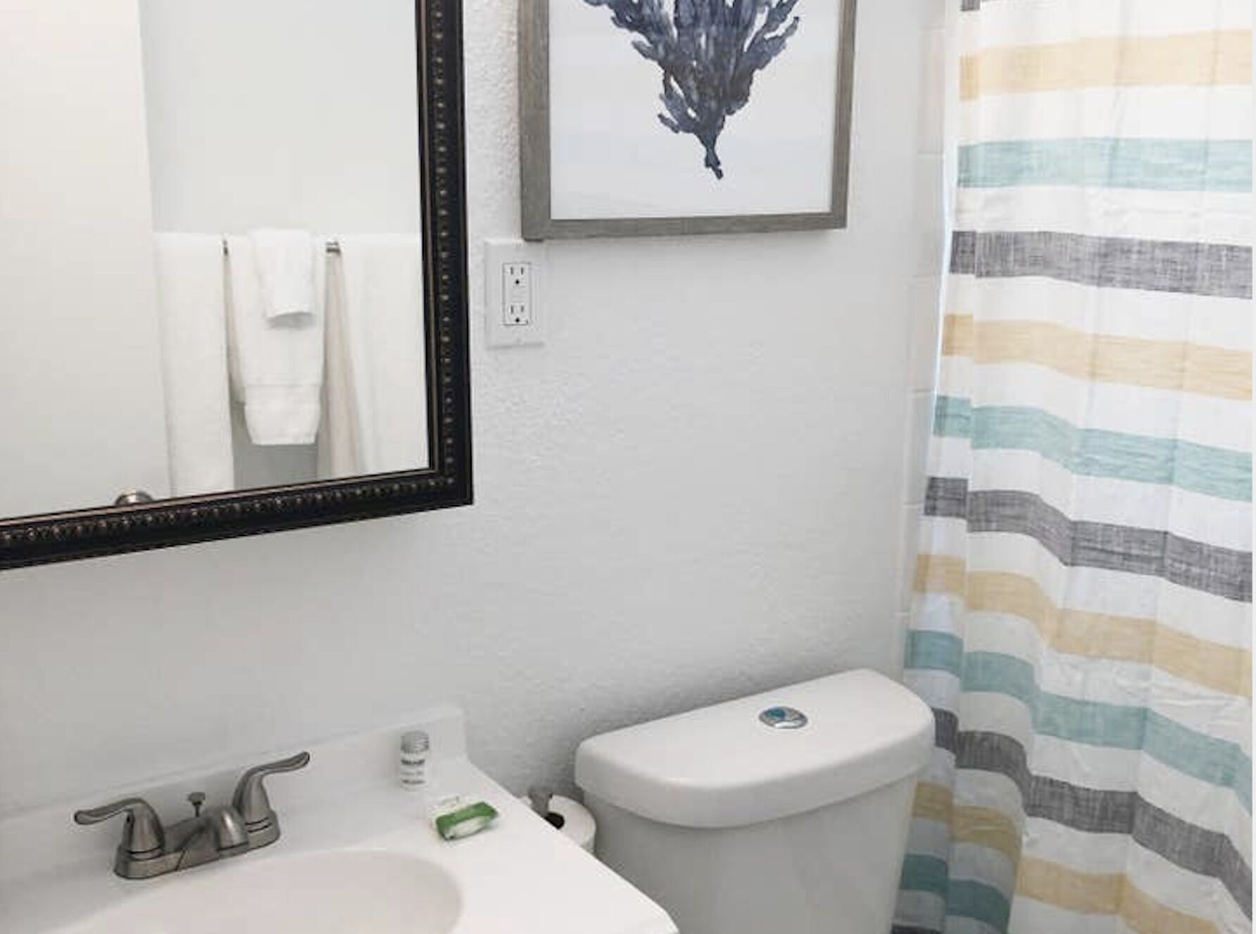 Une salle de bain avec un lavabo blanc, un miroir à cadre noir, des toilettes et un rideau de douche à rayures.