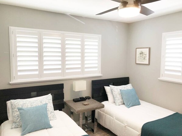 Habitación con dos camas, una mesita, ventilador de techo y un cuadro en la pared.