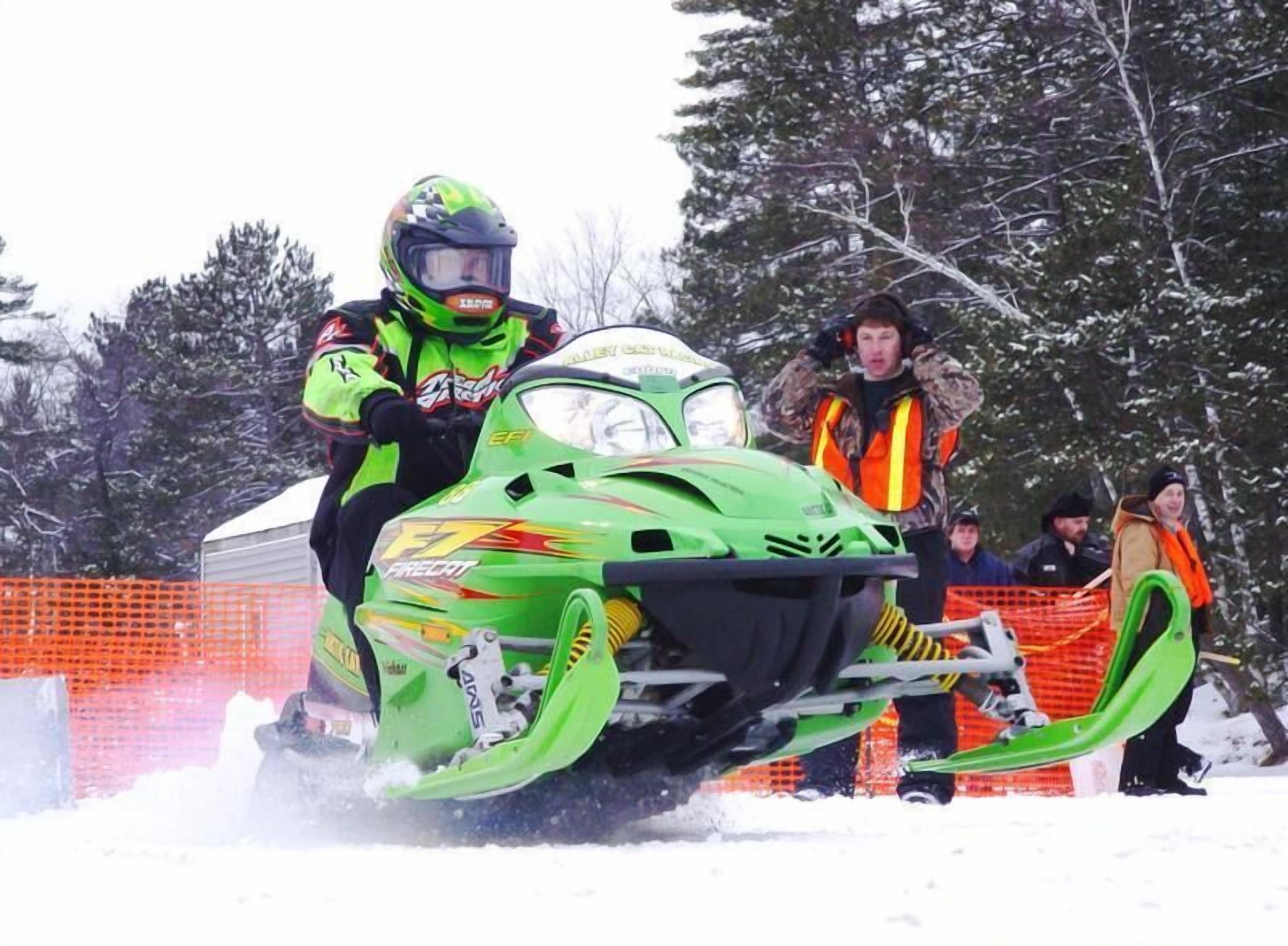 A snowmobile with a driver in a green and black suit.