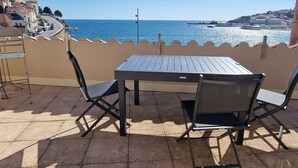 A terrace with a table and chairs overlooking a coastal view.