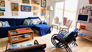 A living room with a blue sofa, a wicker coffee table, a wooden chair, and a television on a stand.