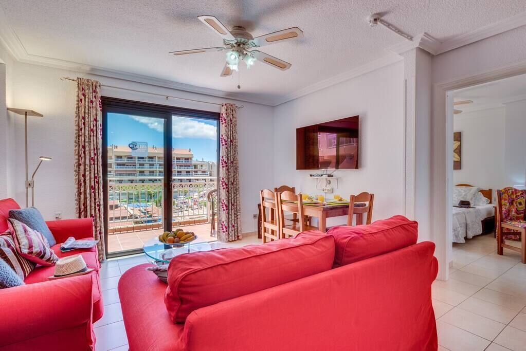 A bright living room with red sofas, a dining table, and a ceiling fan.