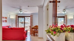 Uma sala de estar com um sofá vermelho, uma mesa de jantar e plantas em vasos.