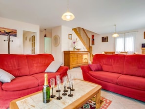A living room with red sofas, a wooden coffee table with wine glasses and a bottle, and a staircase in the background.