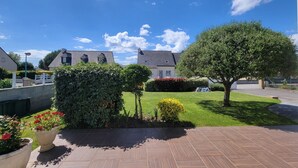 A courtyard with a paved walkway, a large tree, and a building with a sloped roof in the background. - L'Olivier by Interhome (Erdeven)