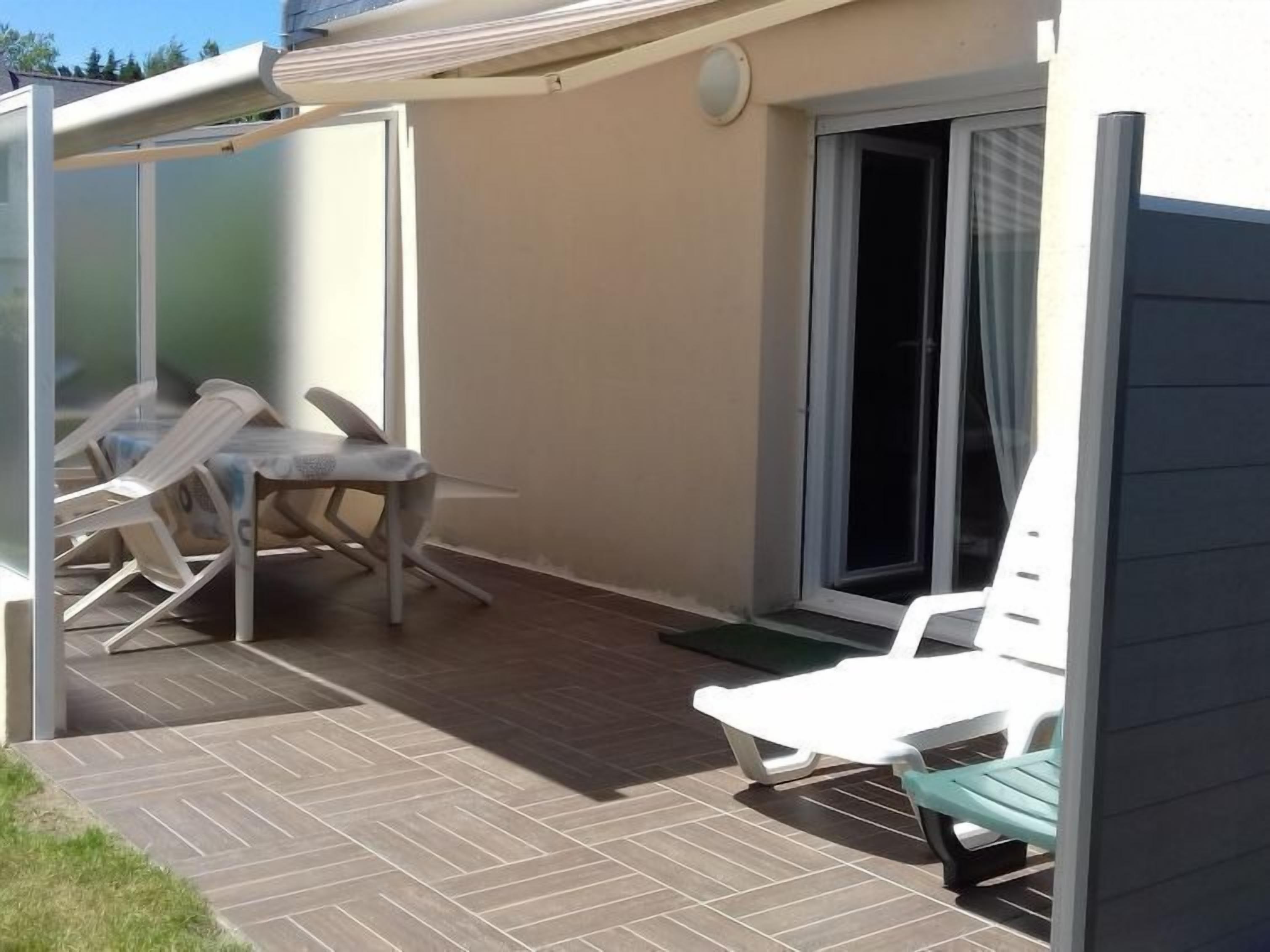 Een overdekt terras met een tafel, stoelen, een schuifpui en een klein, groen kleedje.
