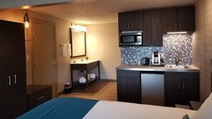 A compact hotel room with a bed, a kitchenette, a bathroom, and a small seating area. - The Hotel Y, a Dazzler Select by Wyndham (YAKIMA)