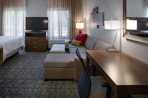 Una habitación de hotel con cama, sofá, escritorio, televisor y lámpara.