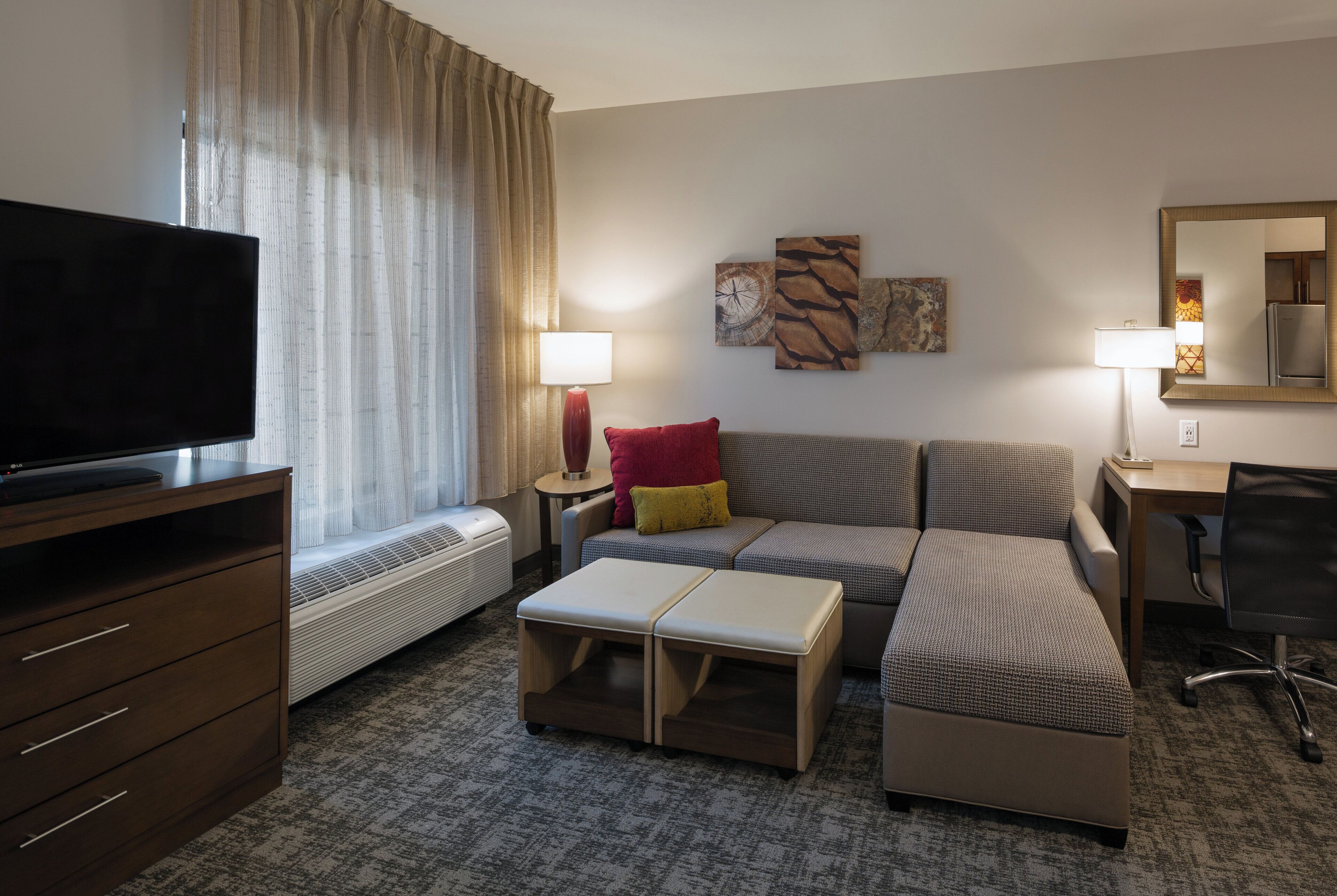 Une chambre d’hôtel équipée d’un téléviseur à écran plat, d’un canapé, d’un bureau, d’une chaise et d’une grande fenêtre avec des rideaux.