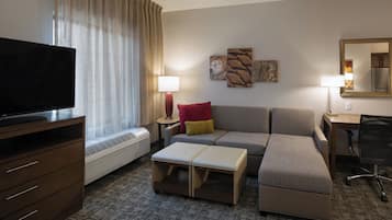 A hotel room with a flat-screen TV, a sofa, a desk, a chair, and a large window with curtains.