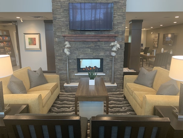 Una sala de estar moderna con chimenea de piedra, dos sofás, una mesa de centro y un televisor montado en la pared.