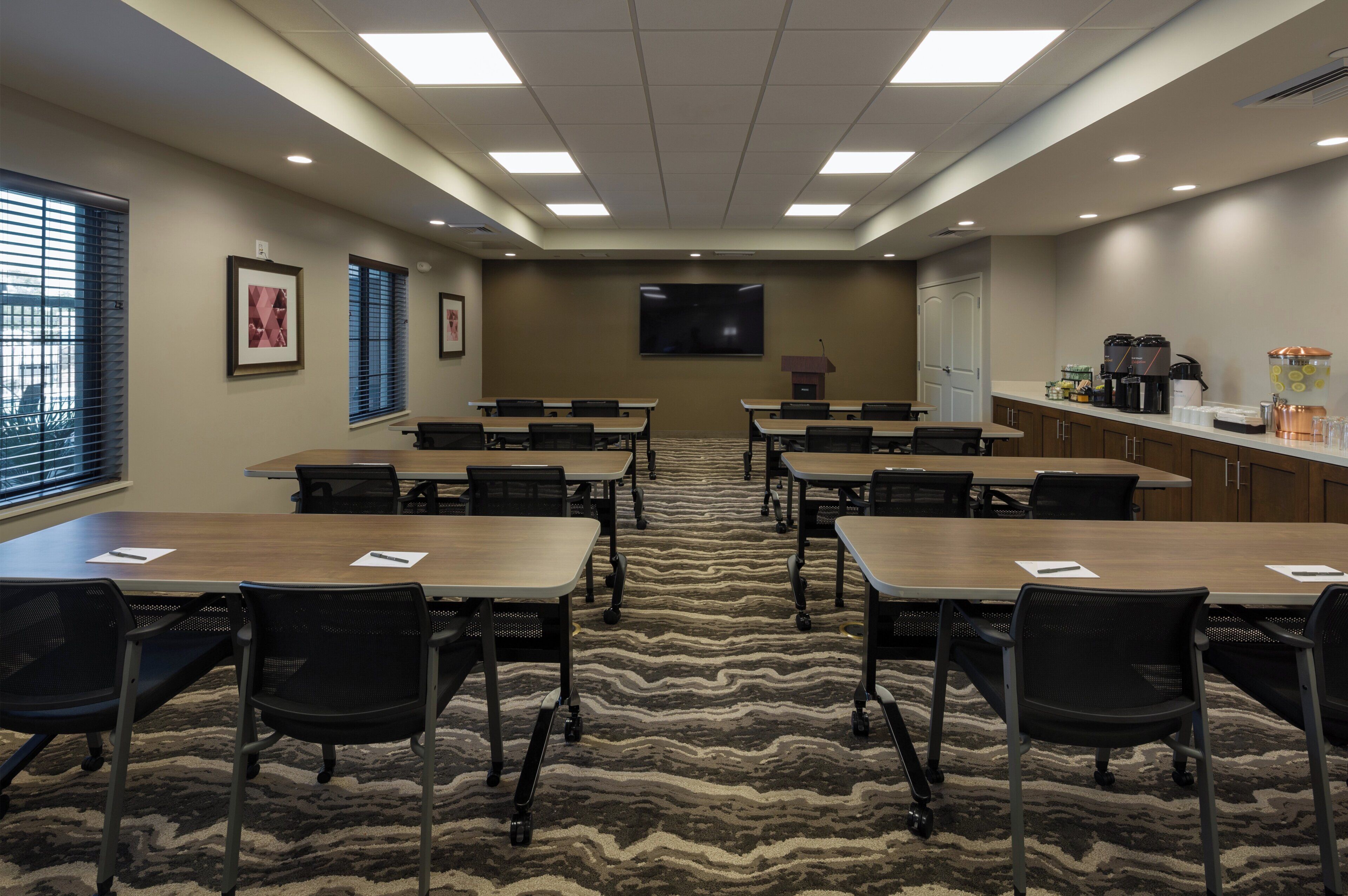 A conference room with a large screen, multiple tables, and chairs.