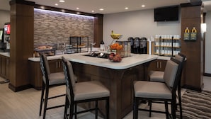 Un espace cuisine moderne doté d’un îlot central, de tabourets de bar, d’un coin café et d’un pare-feu en pierre.