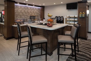 A modern kitchen area with a central island, bar stools, a coffee station, and a stone backsplash. - Staybridge Suites Phoenix - Biltmore Area by IHG (Phoenix)