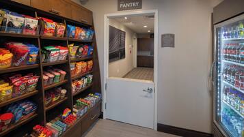 A pantry area with shelves stocked with snacks and a refrigerator with beverages.