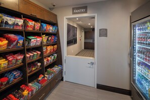 A pantry area with shelves stocked with snacks and a refrigerator with beverages. - Staybridge Suites Phoenix - Biltmore Area by IHG (Phoenix)