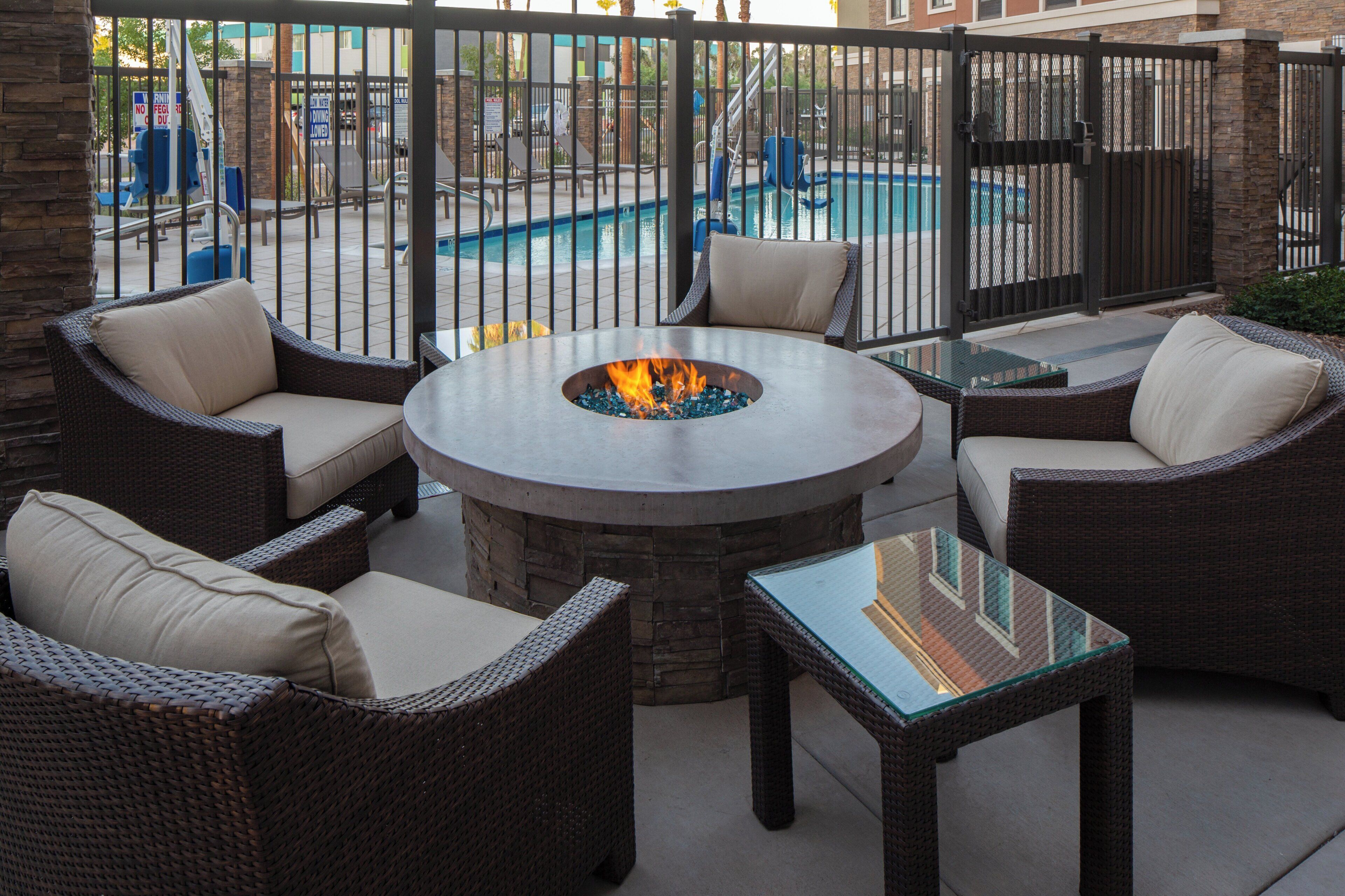 Un patio con mobiliario de mimbre, una mesa con superficie de vidrio y una chimenea en el centro.