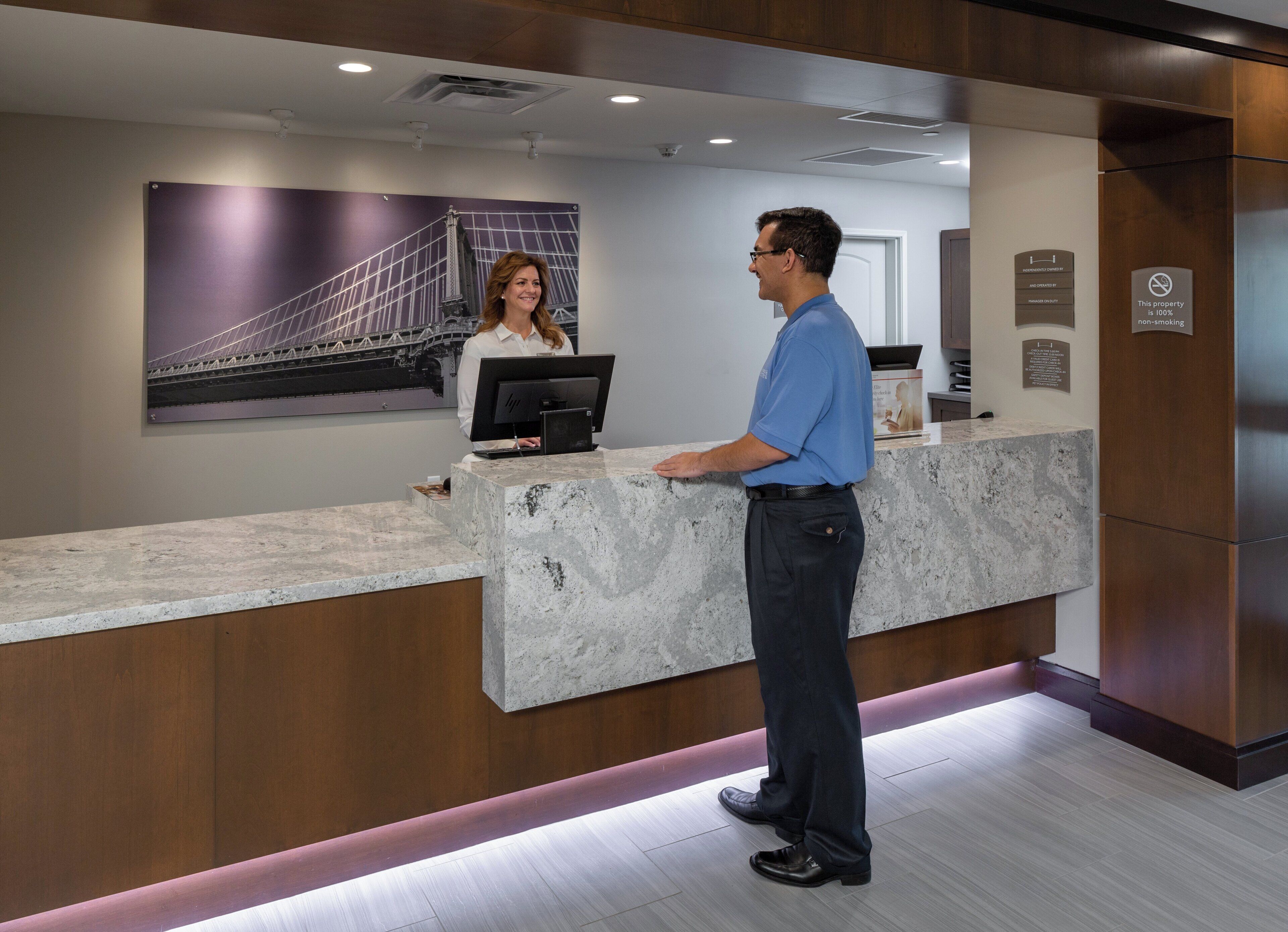 A reception desk with a marble counter, a person standing in front of it, and a woman seated behind the counter.