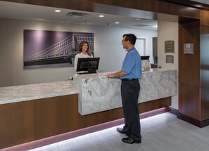 A reception desk with a marble counter, a person standing in front of it, and a woman seated behind the counter. - Staybridge Suites Phoenix - Biltmore Area by IHG (Phoenix)