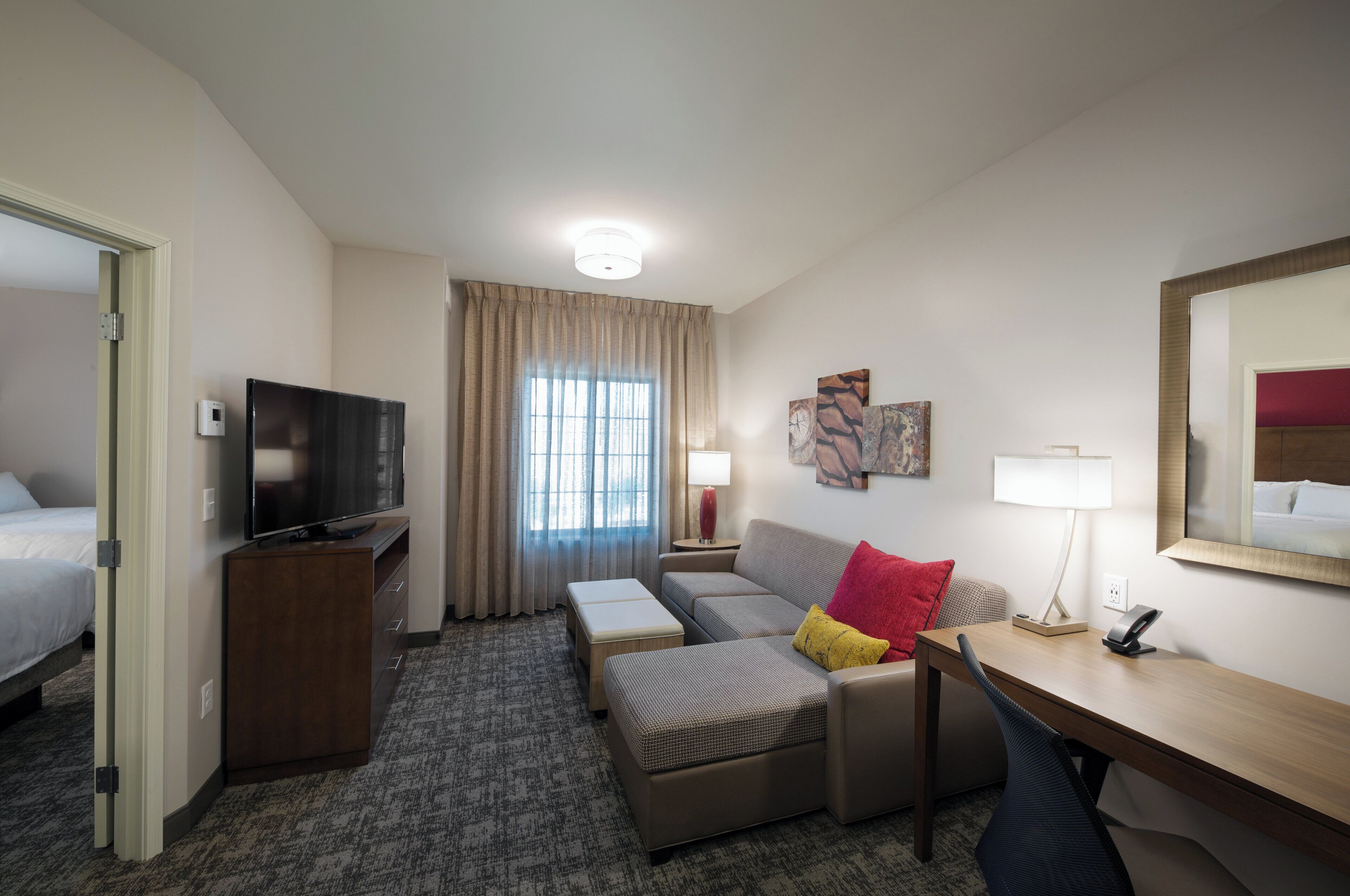 Hotelkamer met een bed, televisie, bureau, stoel, bank, een klein tafeltje, lamp en raam met gordijnen.