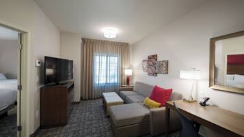 Hotelkamer met een bed, televisie, bureau, stoel, bank, een klein tafeltje, lamp en raam met gordijnen.