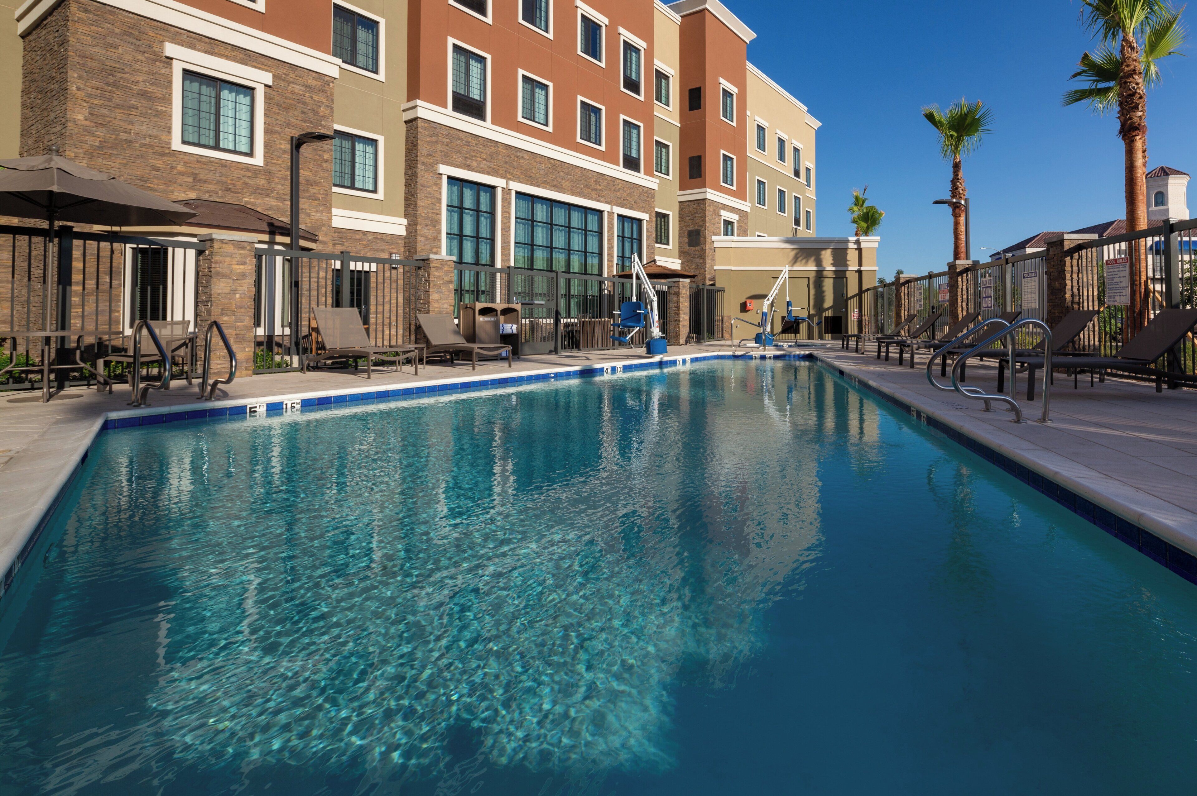 A swimming pool with clear blue water, surrounded by lounge chairs and a building with multiple windows.