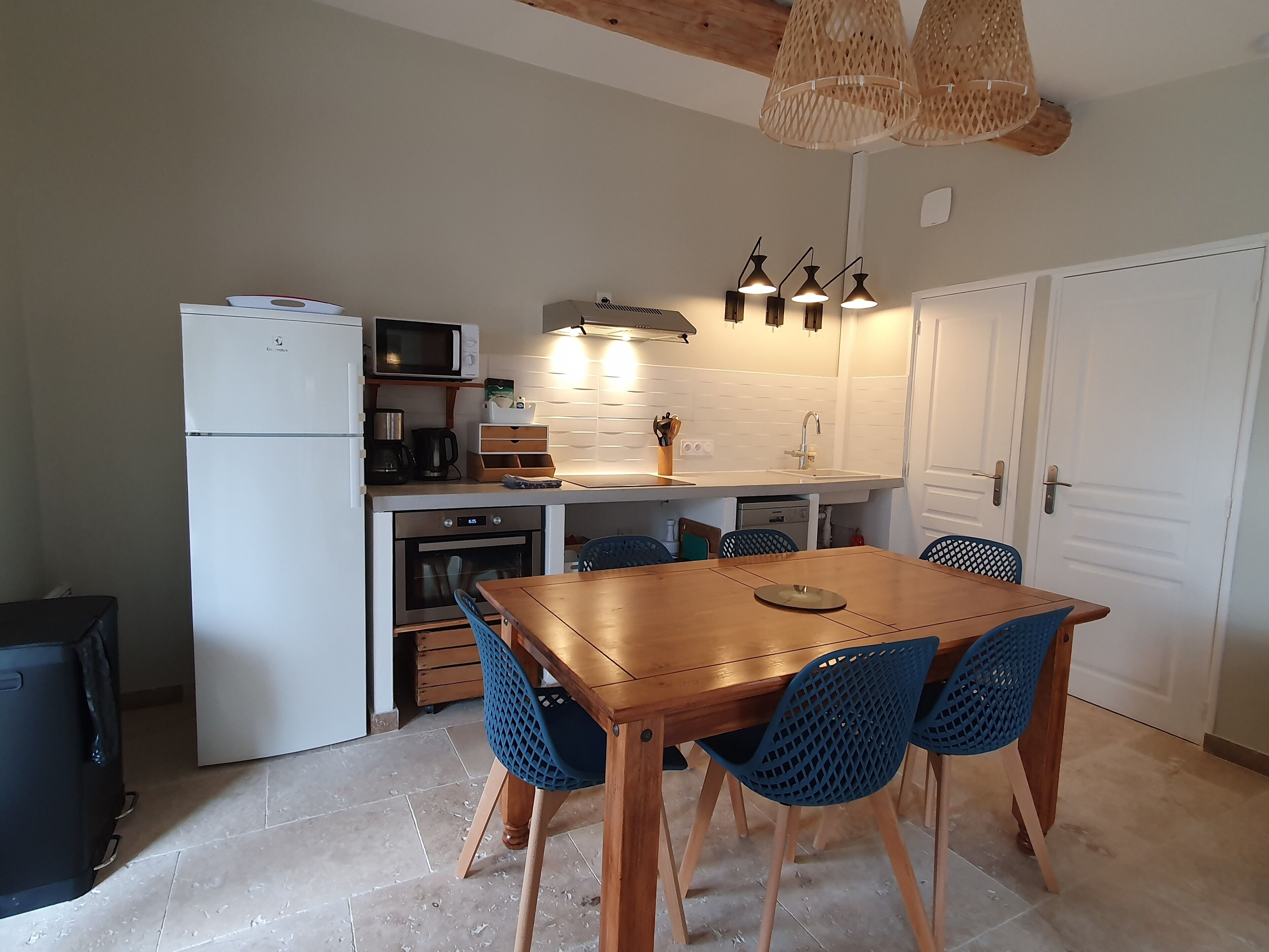 Une cuisine compacte équipée d’un réfrigérateur, d’un four à micro-ondes, d’une cuisinière et d’un évier. On y trouve une table à manger en bois avec des chaises bleues.
