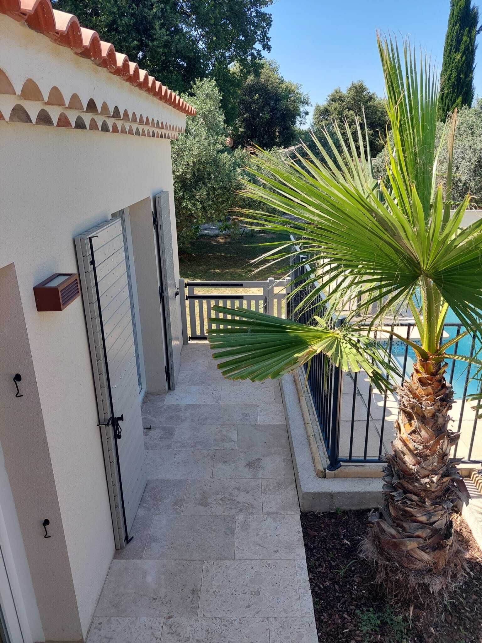 A narrow outdoor corridor with a palm tree and a pool in the background.