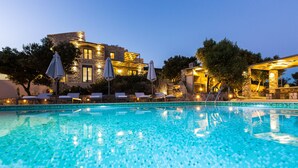 A swimming pool with lounge chairs and umbrellas, surrounded by stone buildings with warm lighting. - Endless Blue View, Top Beaches Nearby (Rethymno)